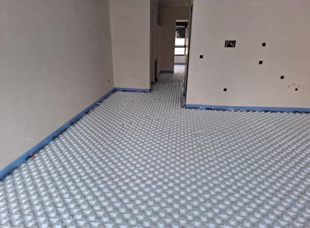 Interior de vivienda en obra con instalación de suelo radiante en proceso.
