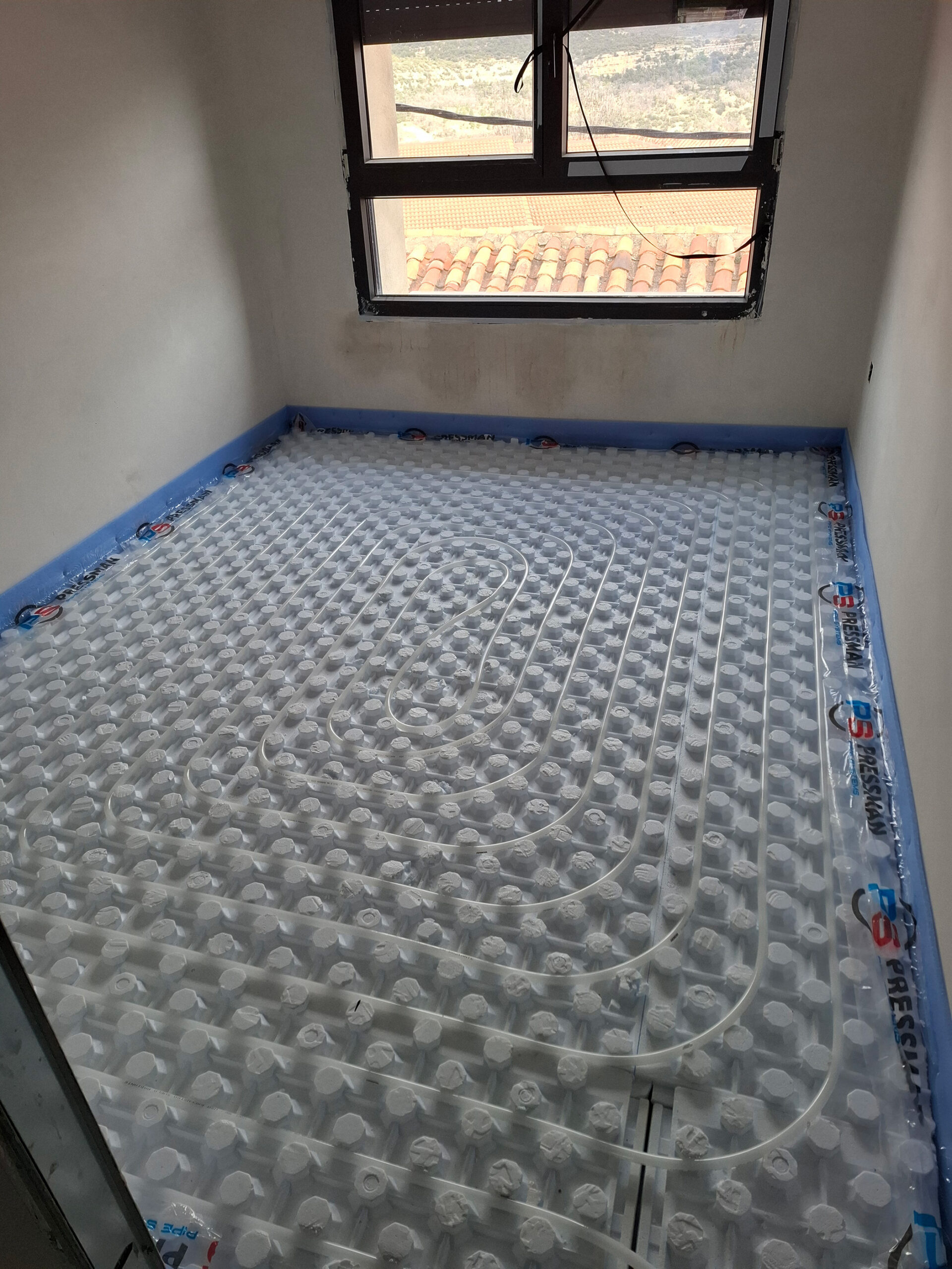 Habitación en obra con instalación de suelo radiante en espiral bajo ventana con vistas.