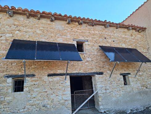 Fachada de casa de piedra con dos grupos de paneles solares fotovoltaicos.