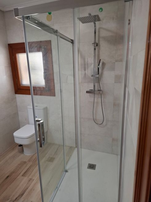 Baño moderno con ducha de obra, mampara de cristal y sanitario de porcelana blanca.