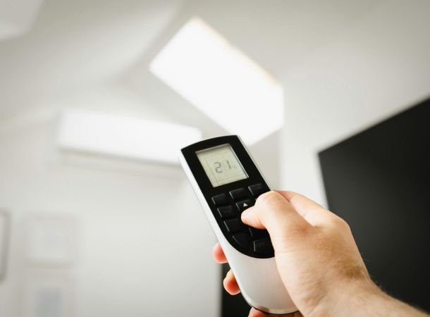 Mano sosteniendo un mando de aire acondicionado con temperatura ajustada a 21 grados.