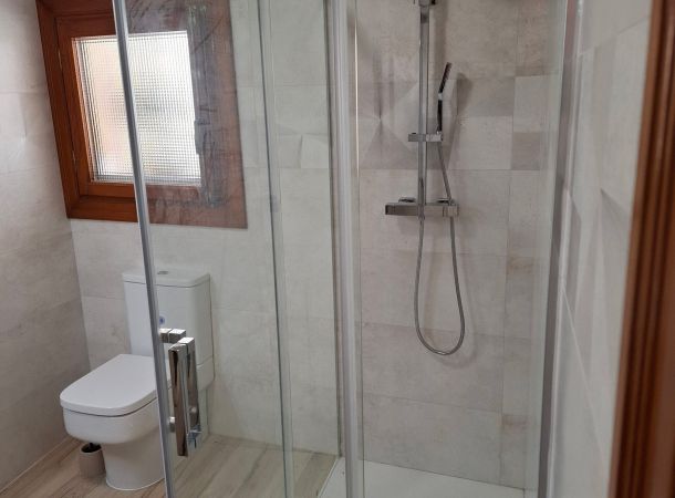Baño moderno con ducha de obra, mampara de cristal y sanitario de porcelana blanca.