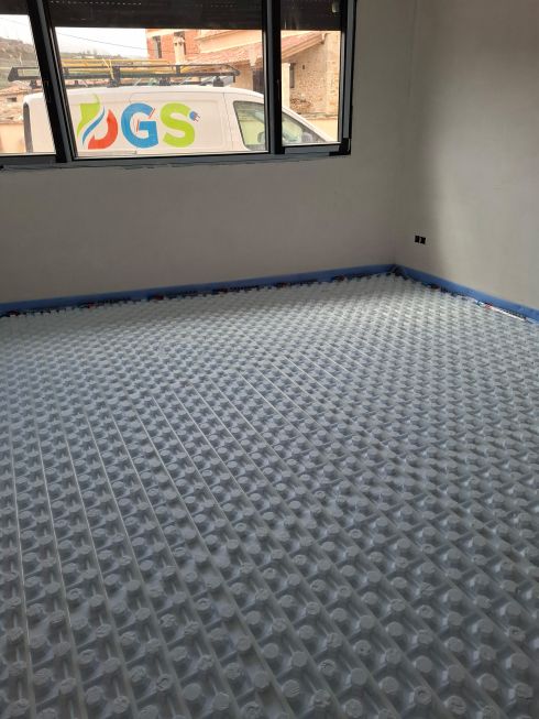 Habitación en obra con suelo radiante instalado y furgoneta de la empresa DGS visible por la ventana.