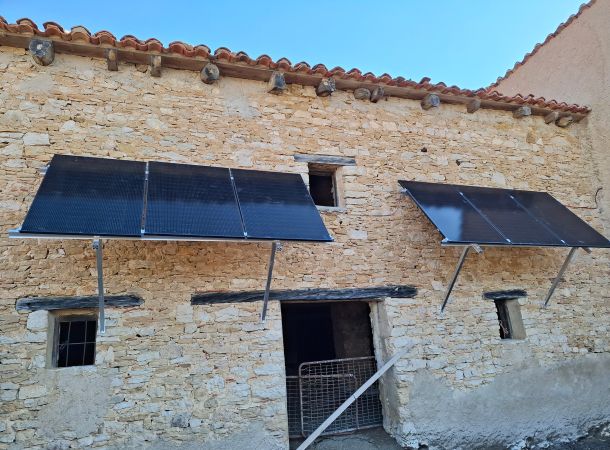 Fachada de casa de piedra con dos grupos de paneles solares fotovoltaicos.
